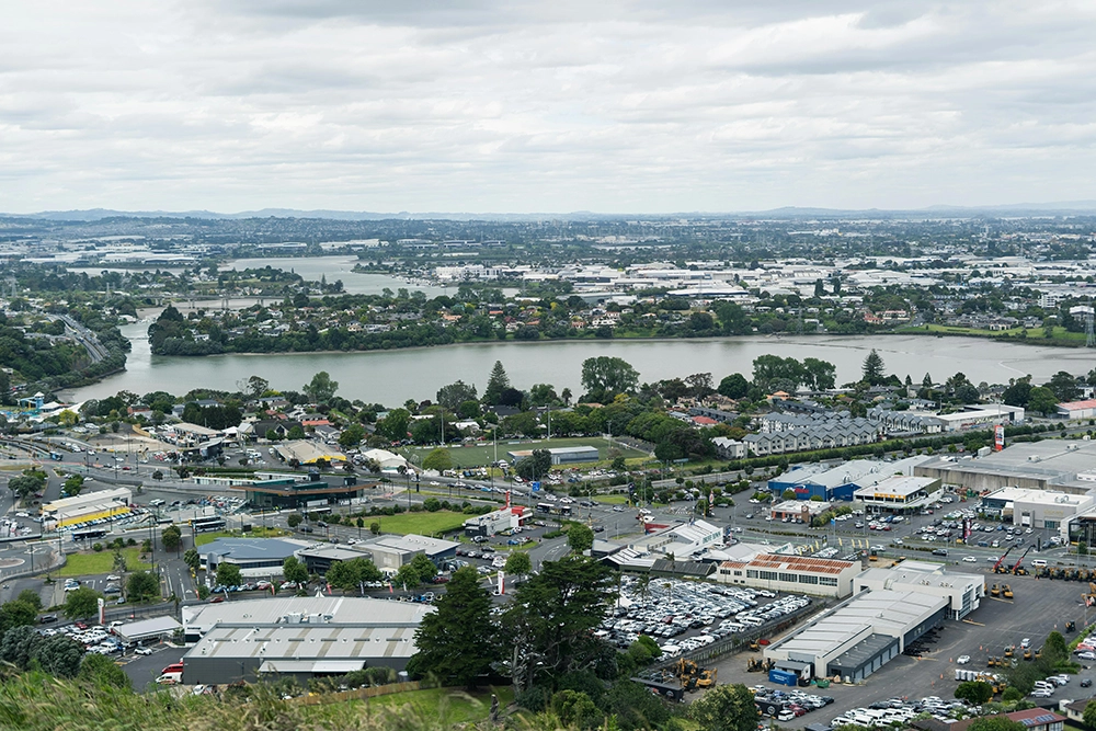 A cityscape view showing a small lake surrounded by residential and industrial buildings under a cloudy sky.
